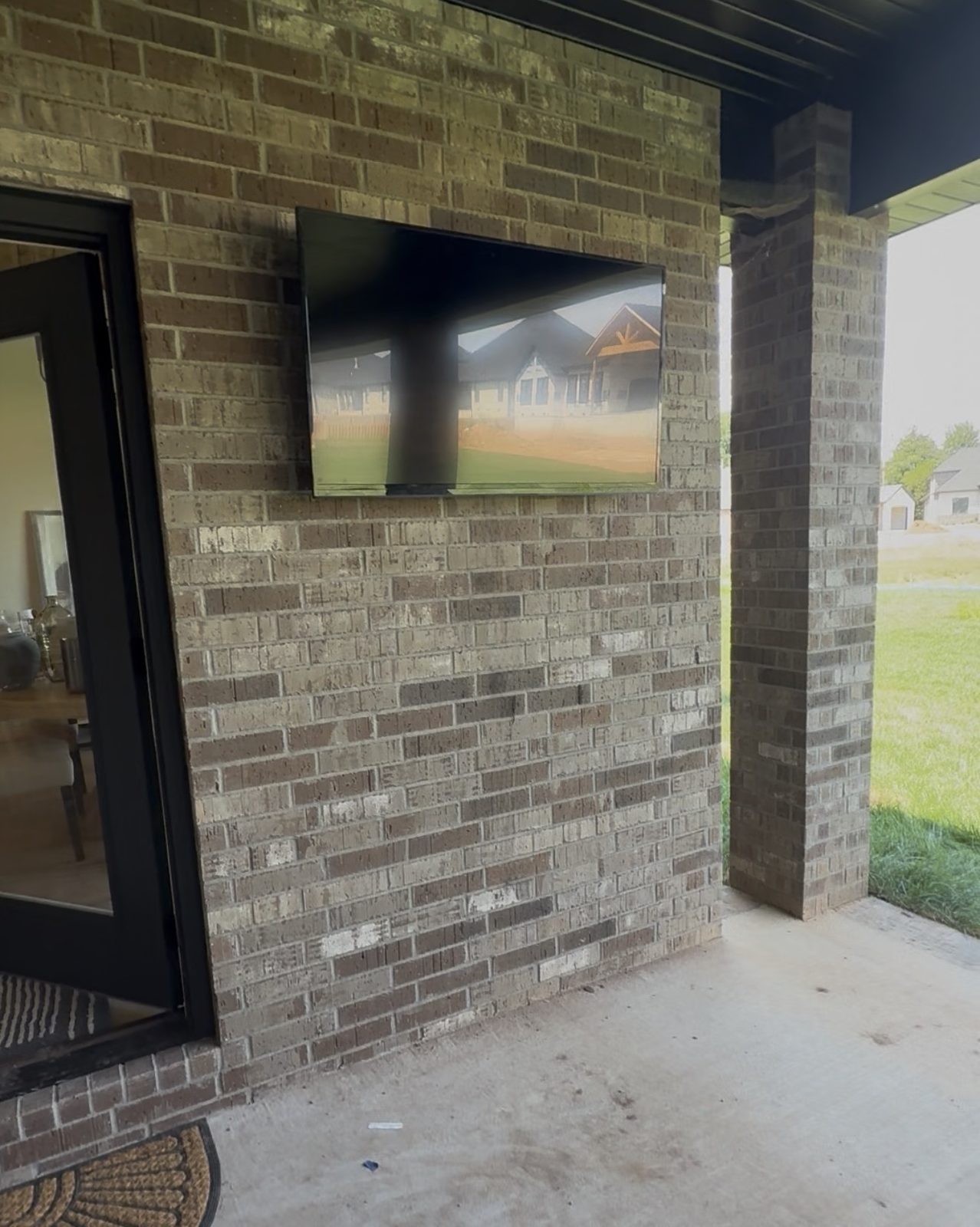 TV mounted on an exterior brick wall under a covered patio
