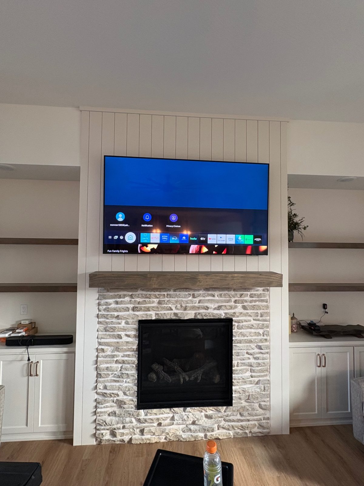 TV mounted over a shiplap and stone fireplace with timber mantel
