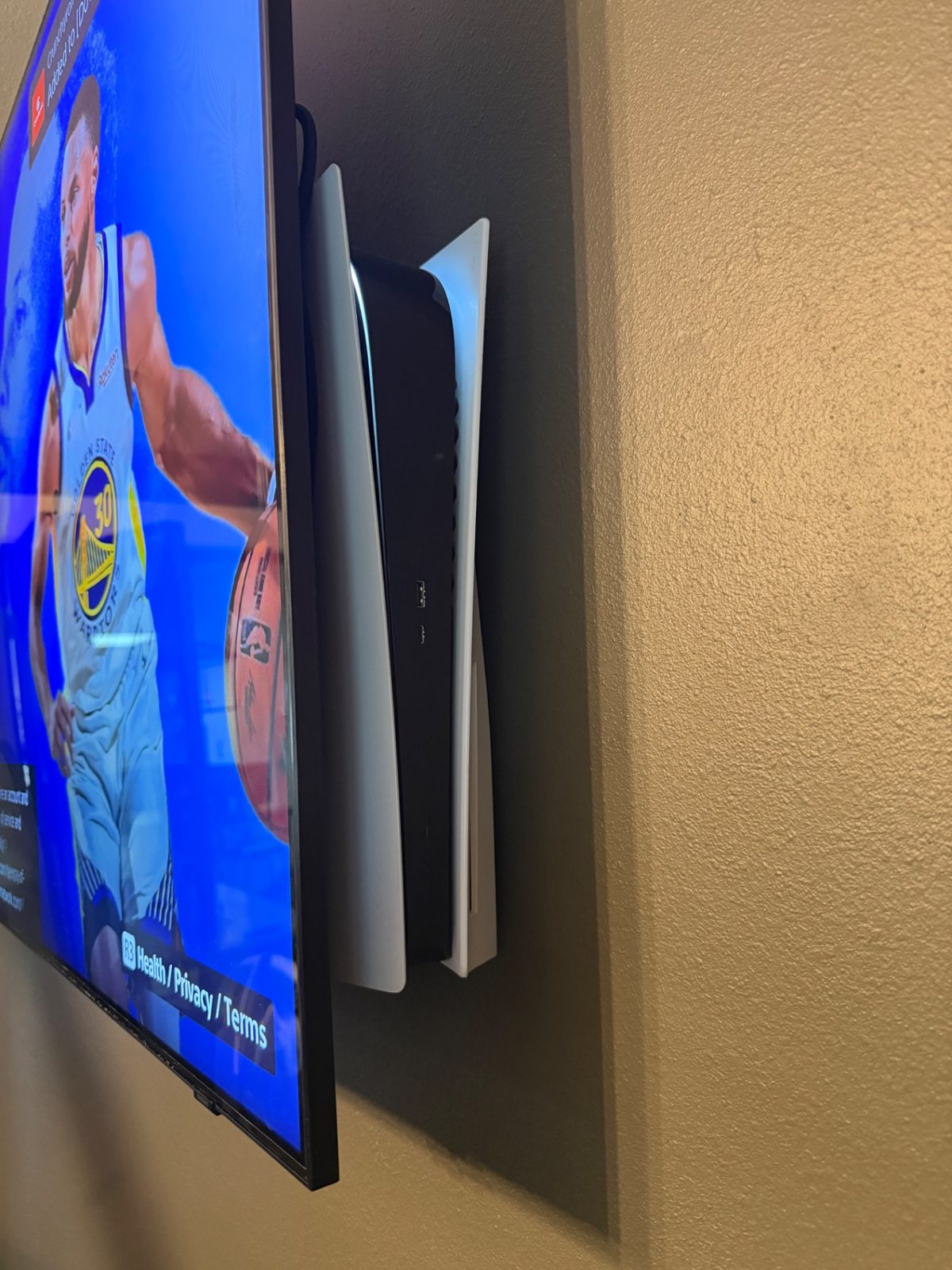 PS5 console mounted on the wall behind a TV