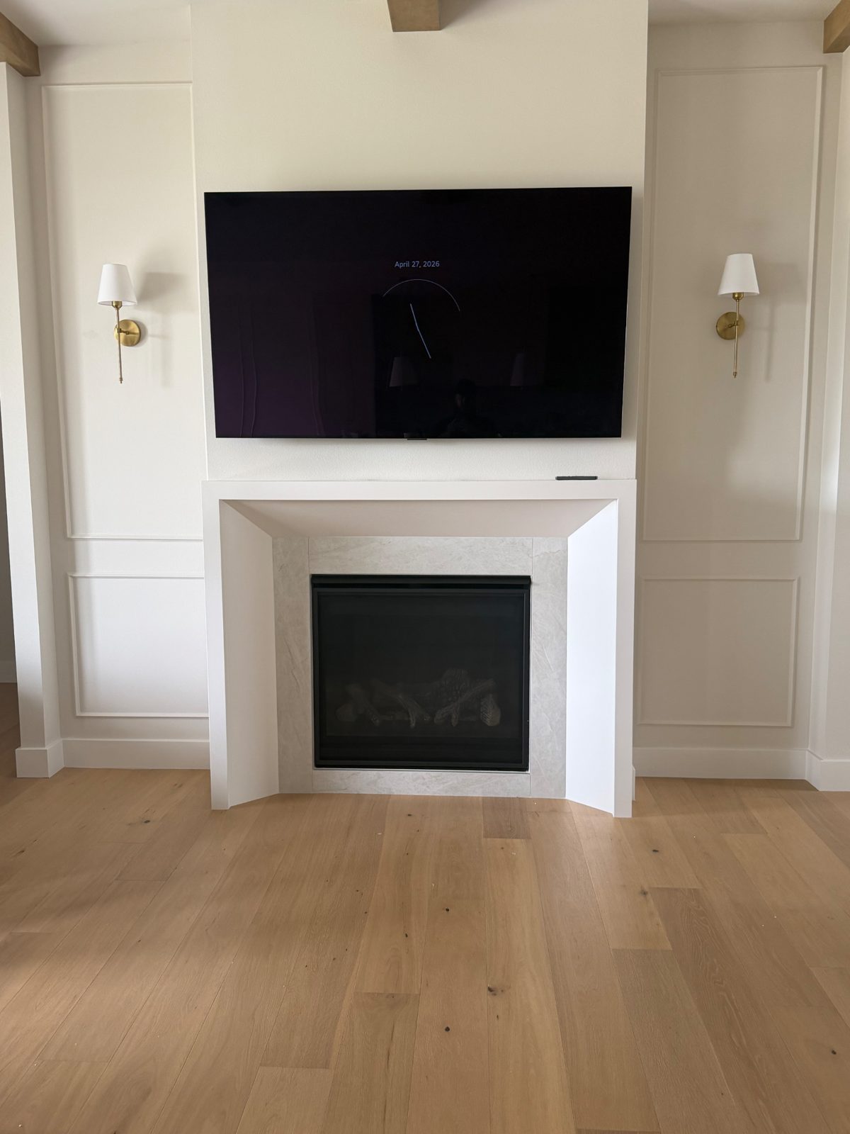 TV centered over a white wainscoting fireplace between wall sconces